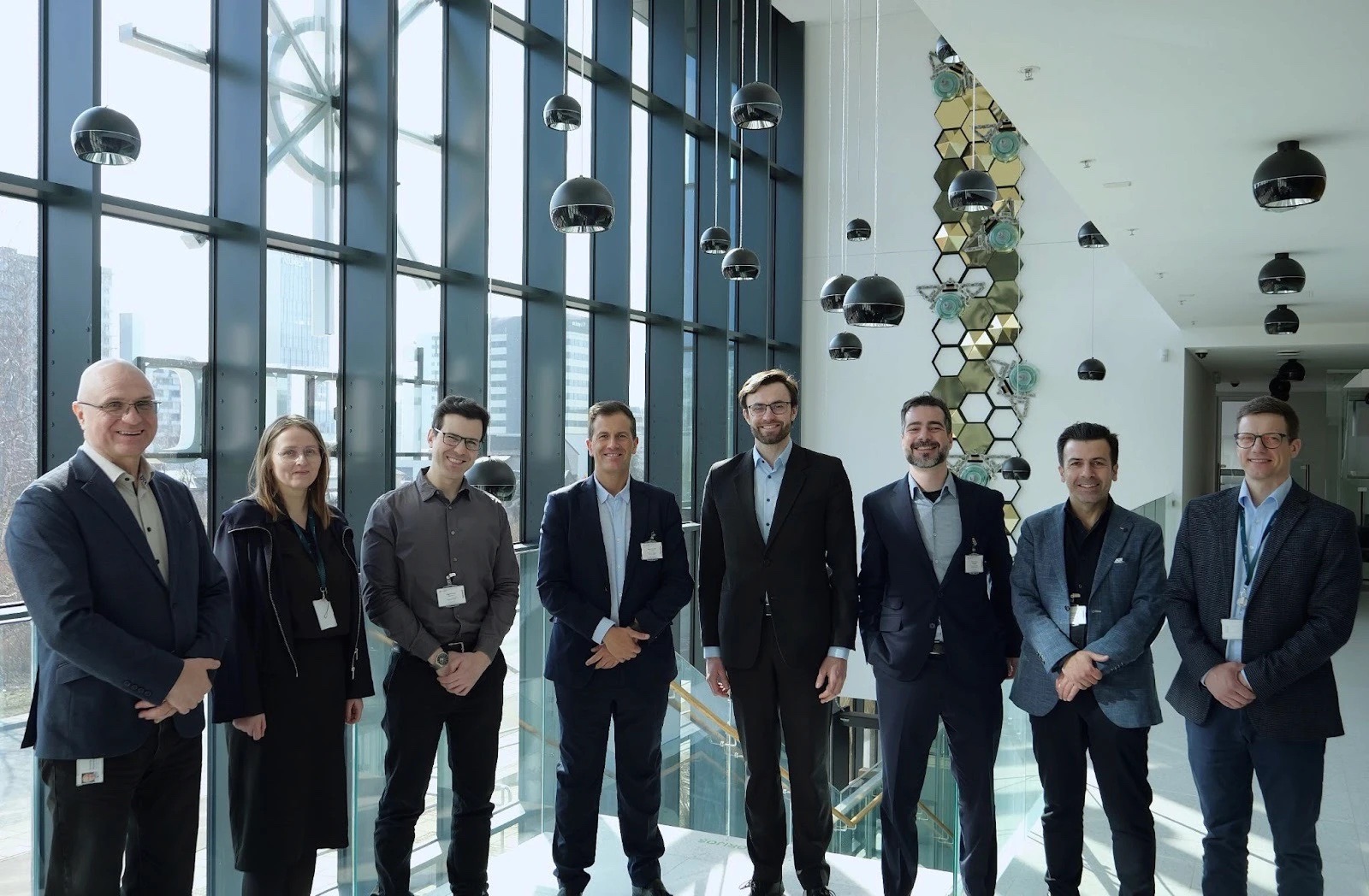 Eight people from the project teams standing together in a glass-walled office atrium